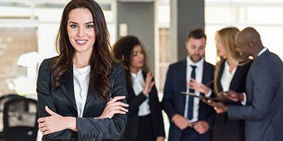 Businesswoman leader looking at camera in modern office with multi-ethnic businesspeople working at the background. Teamwork concept. Caucasian woman.
